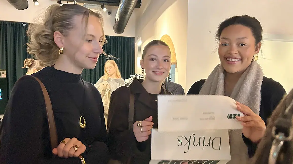 Drei Studentinnen halten einen Flyer und lesen gemeinsam.