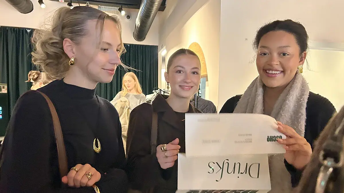 Drei Studentinnen halten einen Flyer und lesen gemeinsam.