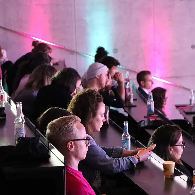 Das Publikum der add conference sitzt im gestuften, violett und hellblau beleuchteten Hörsaal. 