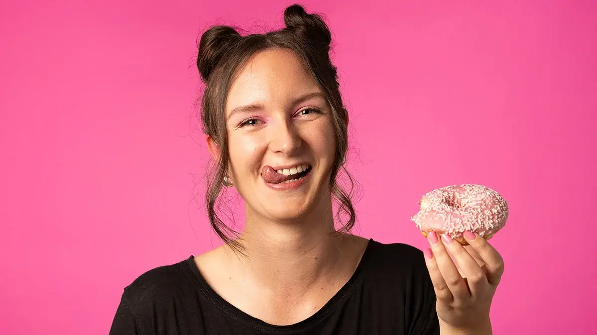 Eine junge Frau hält einen süßen Donut in der Hand und lacht.
