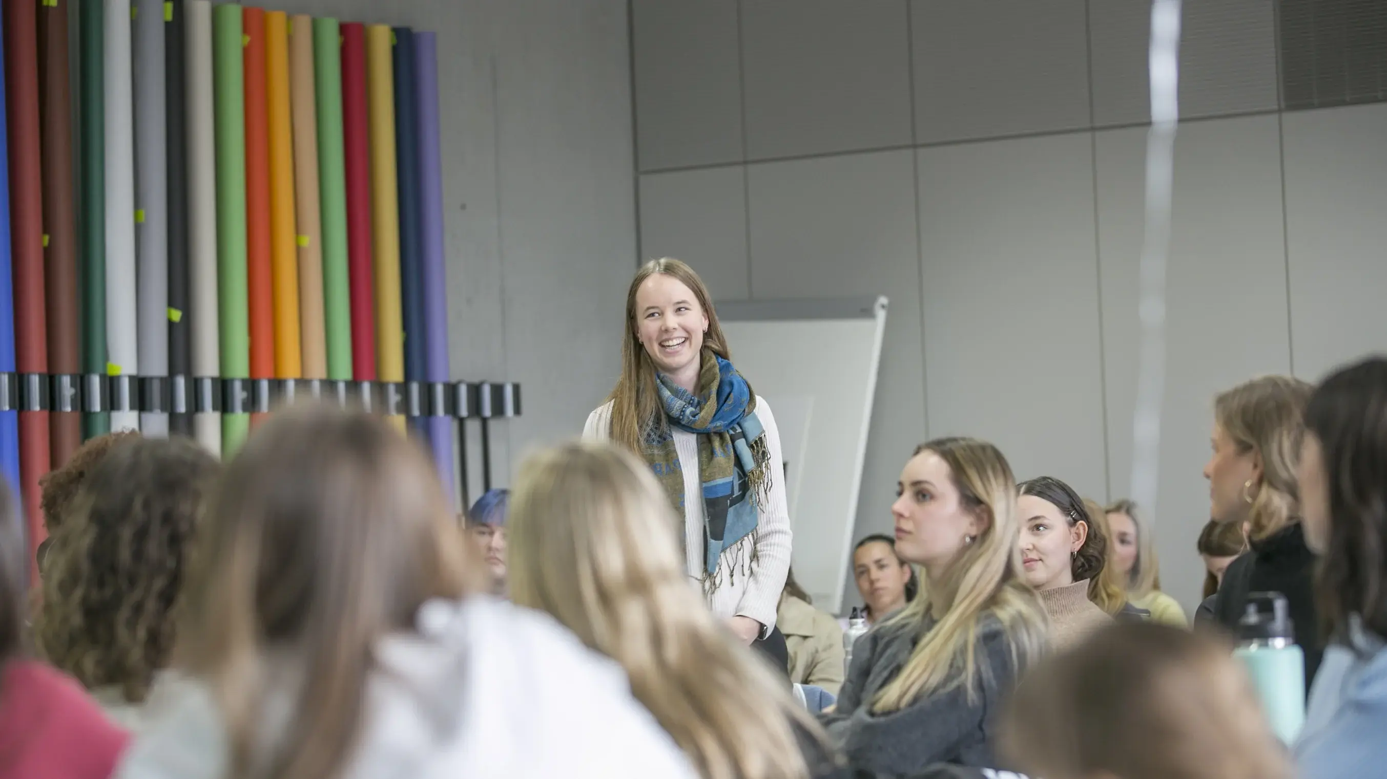 Eine Studentin steht im Hörsaal und stellt sich den anderen Studierenden vor.
