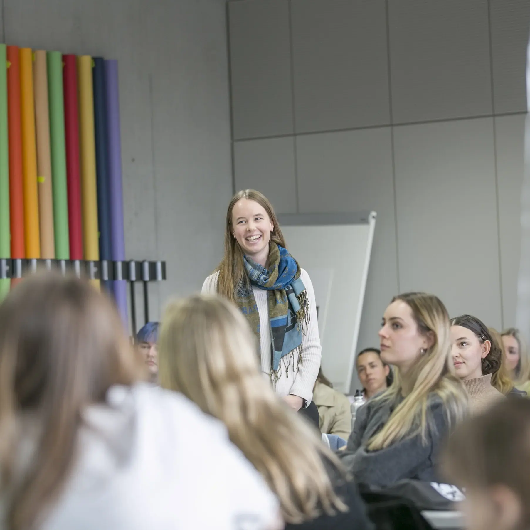 Eine Studentin steht im Hörsaal und stellt sich den anderen Studierenden vor.