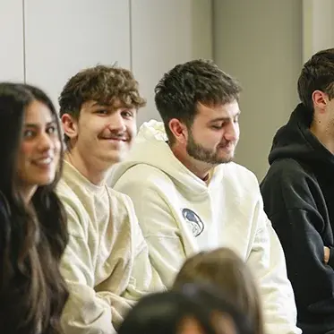 Vier junge Studenten und eine Studentin sitzen bei der Begrüßung auf einem Tisch im Hörsaal.