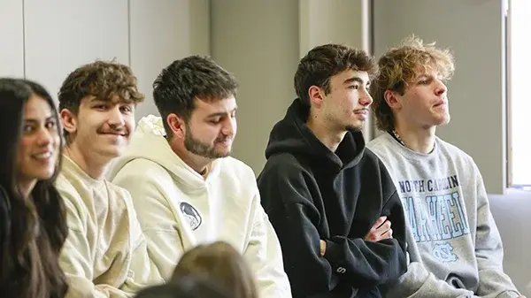 Vier junge Studenten und eine Studentin sitzen bei der Begrüßung auf einem Tisch im Hörsaal.