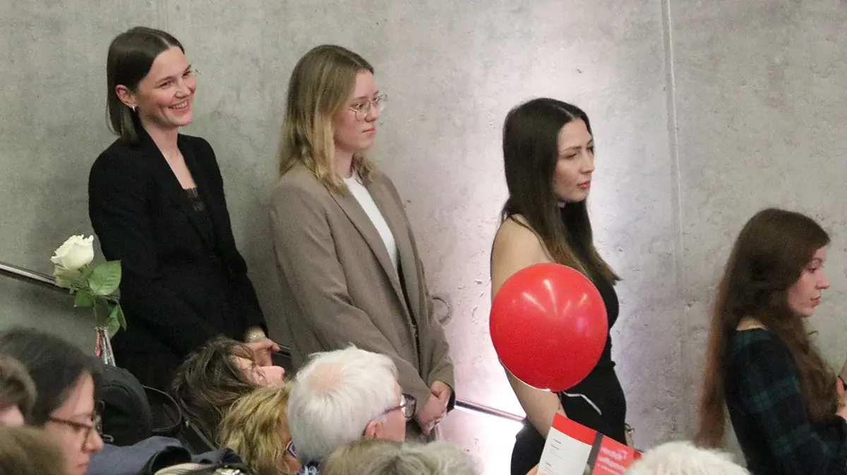 Drei Absolventinnen warten auf die Mappenübergabe.