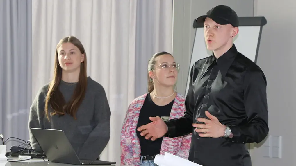 Drei Studierende stehen im Hörsaal am Pult und tragen ihre Ideen vor.