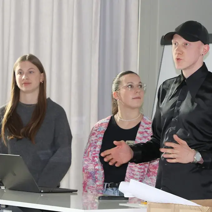 Drei Studierende stehen im Hörsaal am Pult und tragen ihre Ideen vor.