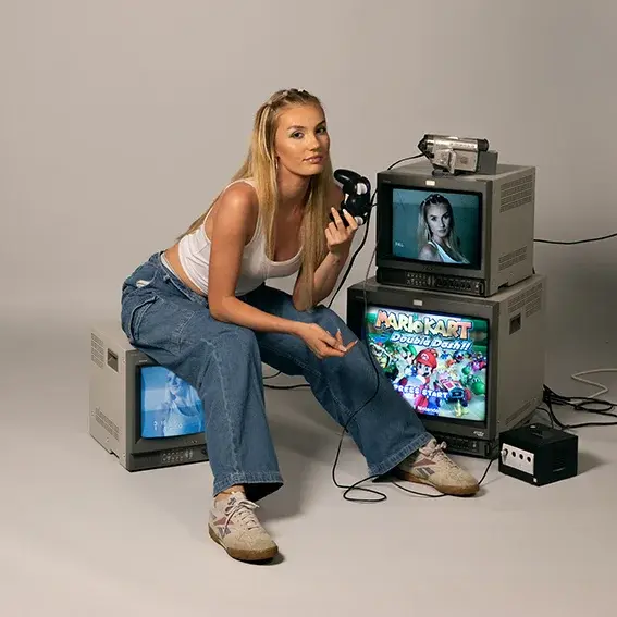 A young woman is sitting in front of an old tube television. There are two other TV sets next to her.