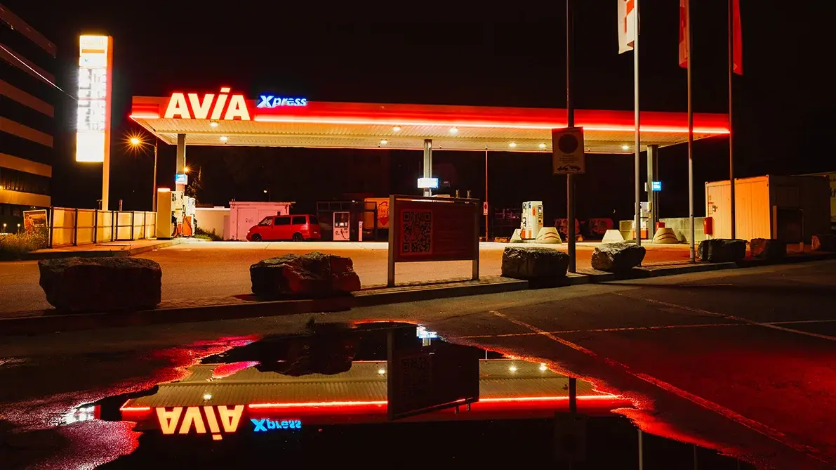 Eine Tankstelle in der Dunkelheit. Ihre Licht spiegelt sich auf dem nassen Asphalt.