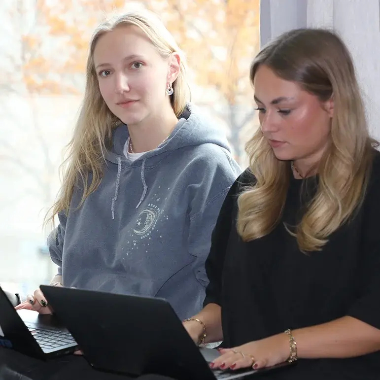 Zwei Studentinnen sitzen mit ihren Laptops am Fenster im Hörsaal.