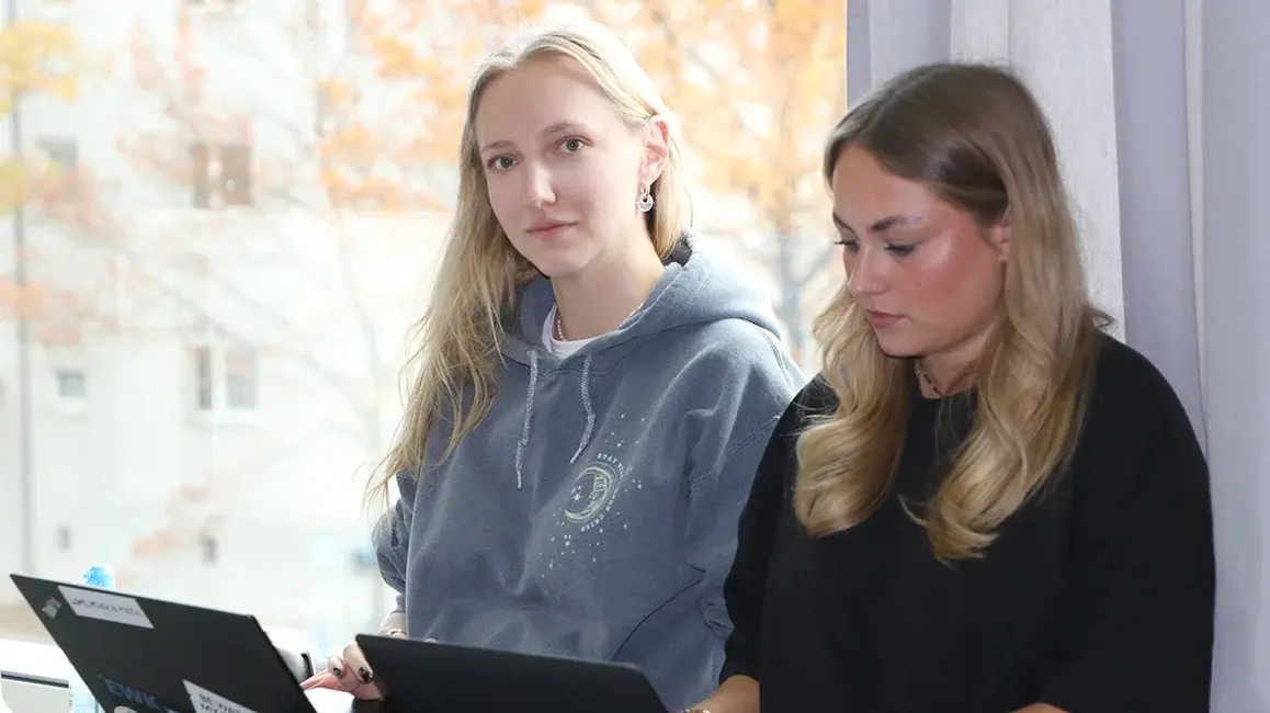 Zwei Studentinnen sitzen mit ihren Laptops am Fenster im Hörsaal.